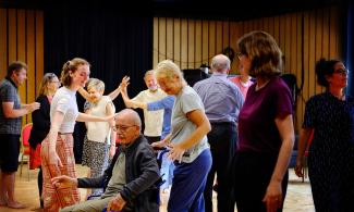 A group of people stand and dance together in a room at Cambridge Junction.