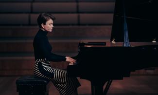 A woman dressed in black, playing a grand piano.