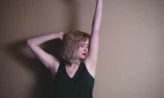 A woman with blonde hair, raising her right arm above her head.