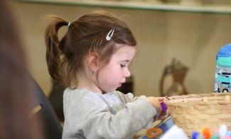 alt= "a young girl with long brown hair tied in a ponytail plays with arts and crafts supplies"