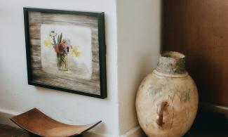 A corner of the Kettle's Yard house. The image is focused on a painting of flowers, hung close to the floor, beneath a window.