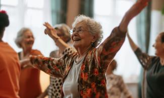 An older lady dances with her hands outstretched in a room of others dancing.