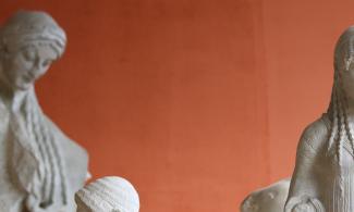 Image of white sculptures of people against a red background.