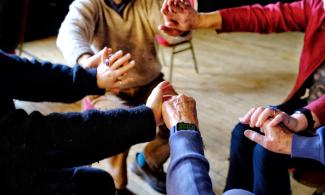 A group of four people sitting in a circle reaching out their arms to one another.