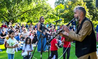 A clarinetist performs in front of children and adults in a garden setting.