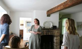 A woman smiling and welcoming two visitors in the Kettle's Yard house.