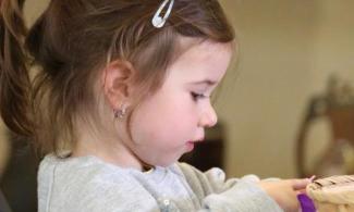 A young girl with her hair in a ponytail with hair clip sits playing at a table of craft materials.
