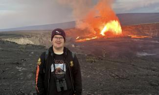 Julian Pahl, a volcanology from the University of Cambridge Department of Earth Sciences, is standing and smiling next to an active volcano in Hawaii.