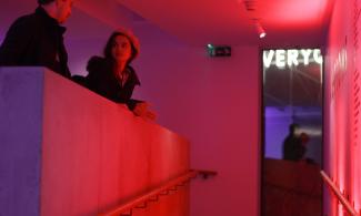 A man and woman talking in a room lit with neon lights