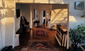 Sunlight casts window shadows across white walls and red patterned rugs on the wooden steps and floor of the Kettle’s Yard house.
