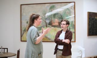 Two people talking in the Kettle’s Yard house, one gesturing with their hands, in front of a large landscape painting.