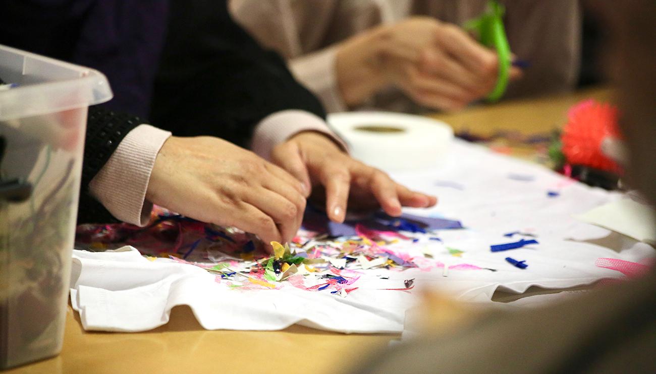 A woman's hand arrange a design on a white t-shirt laying flat on a wooden table.