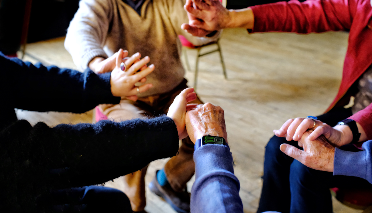 A group of four people sit in a circle holding hands.