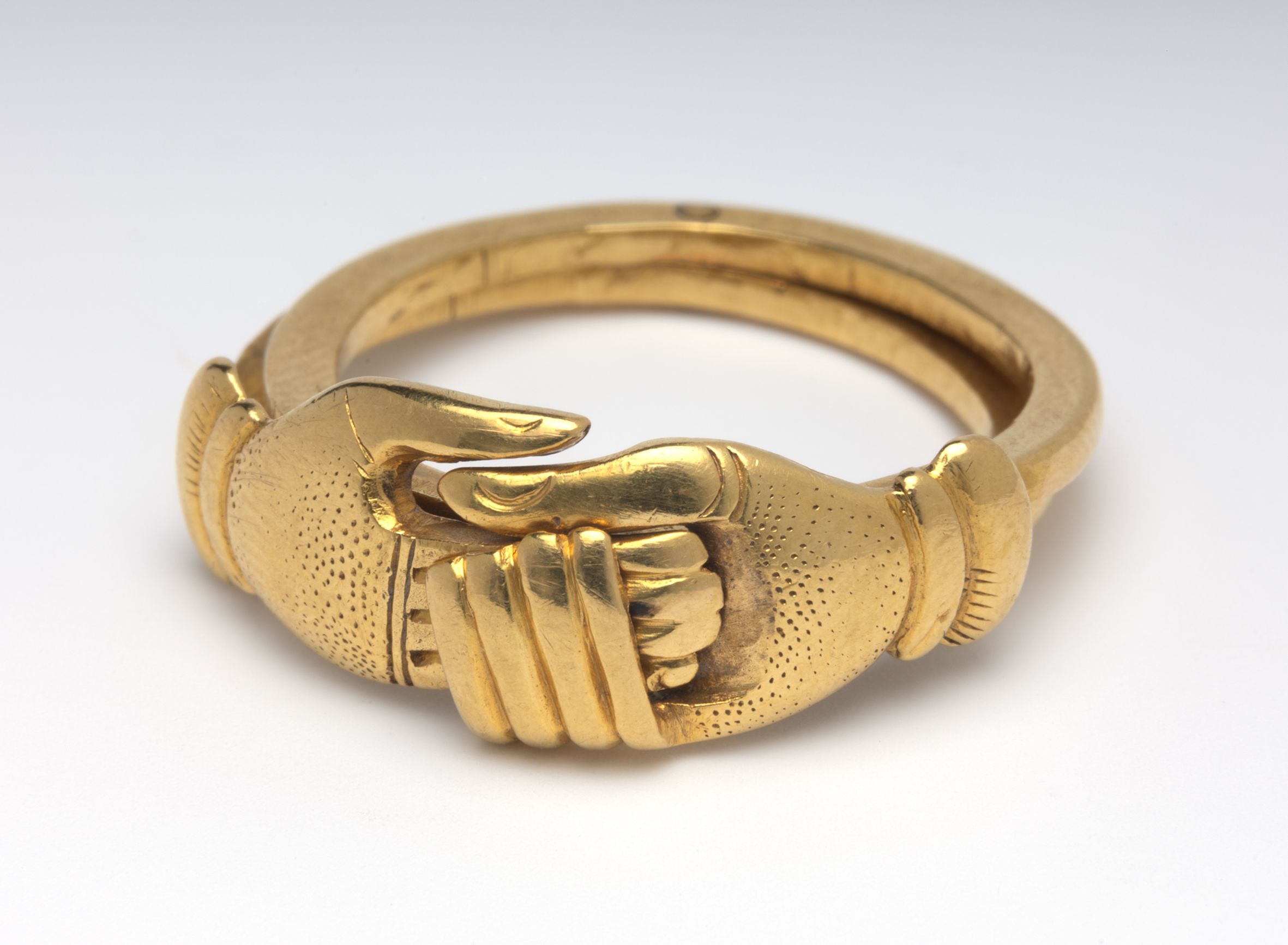 a gold ring formed in the shape of two hands wearing fingerless gloves clasped together