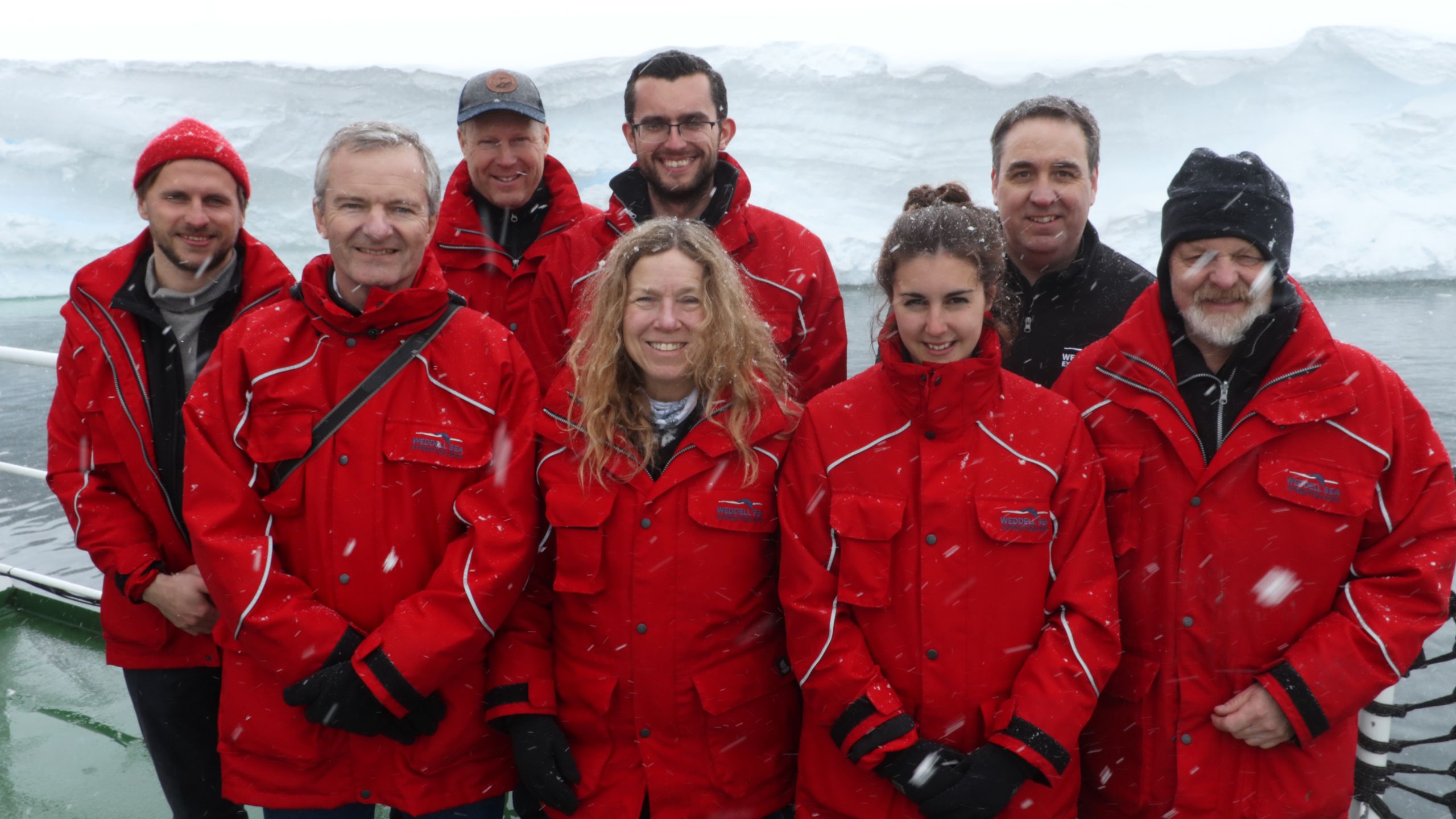 Eight researchers, including Professor Julian Dowdeswell, stand in front of an iceberg.