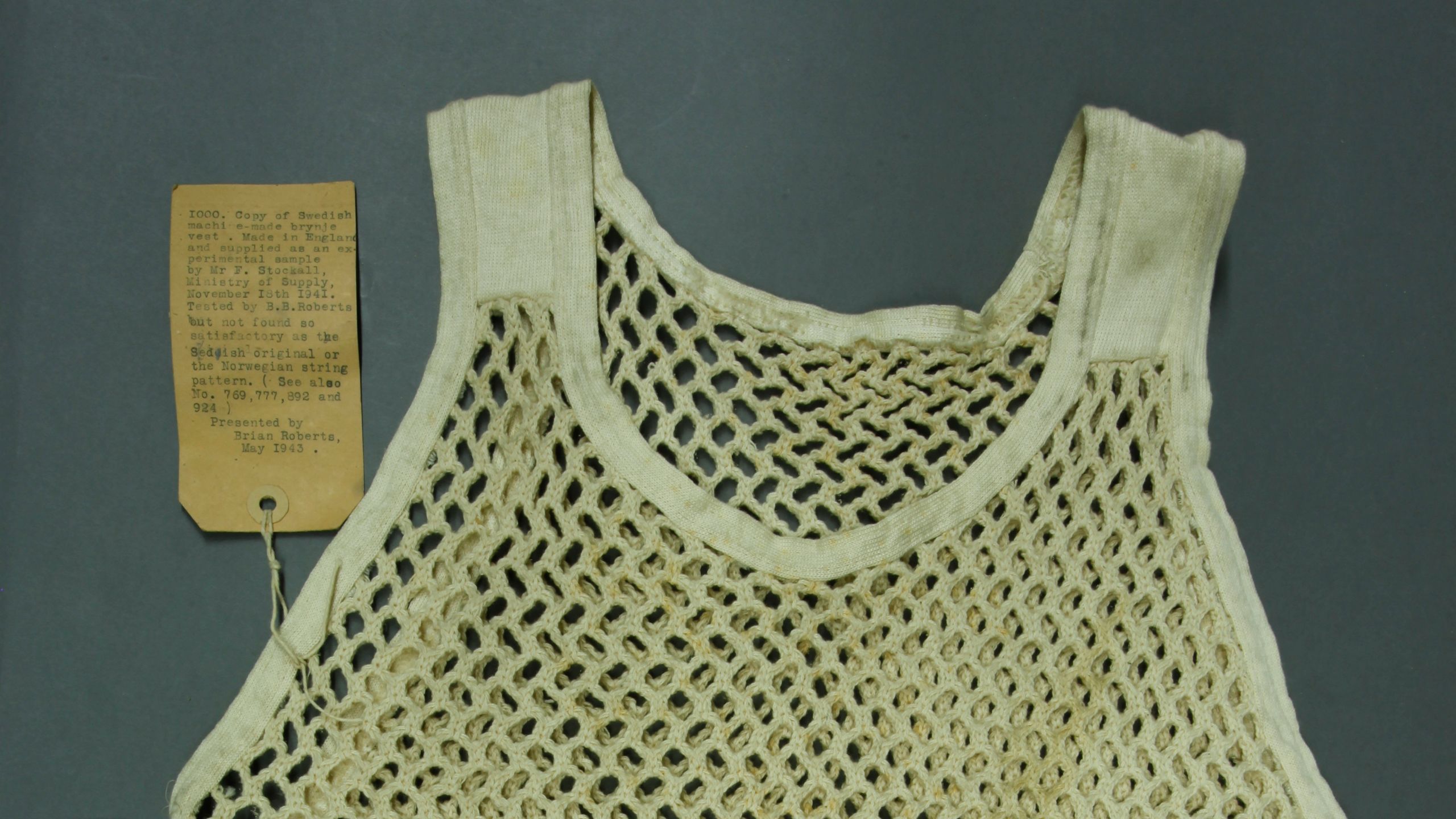 Photograph of a string vest with a museum label attached.