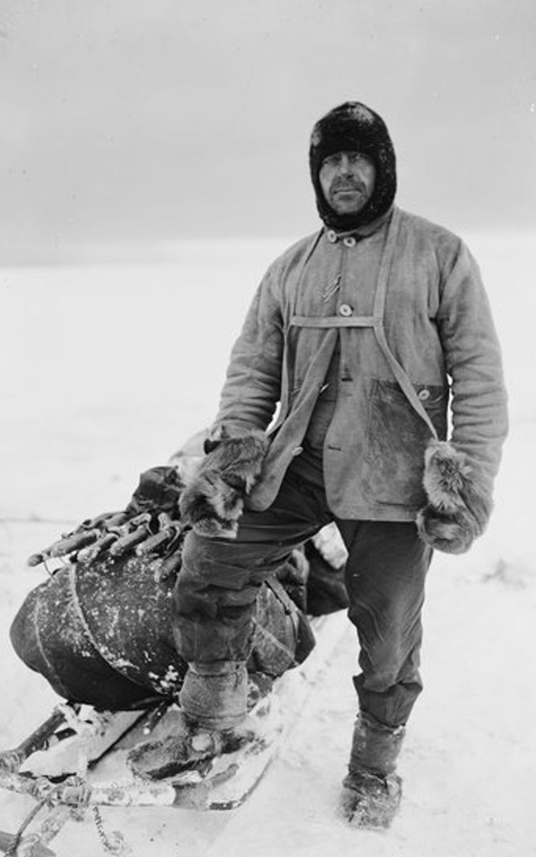 Captain Scott standing on the ice dressed for sledging, including a balaclava, sledging harness, mittens and warm boots.