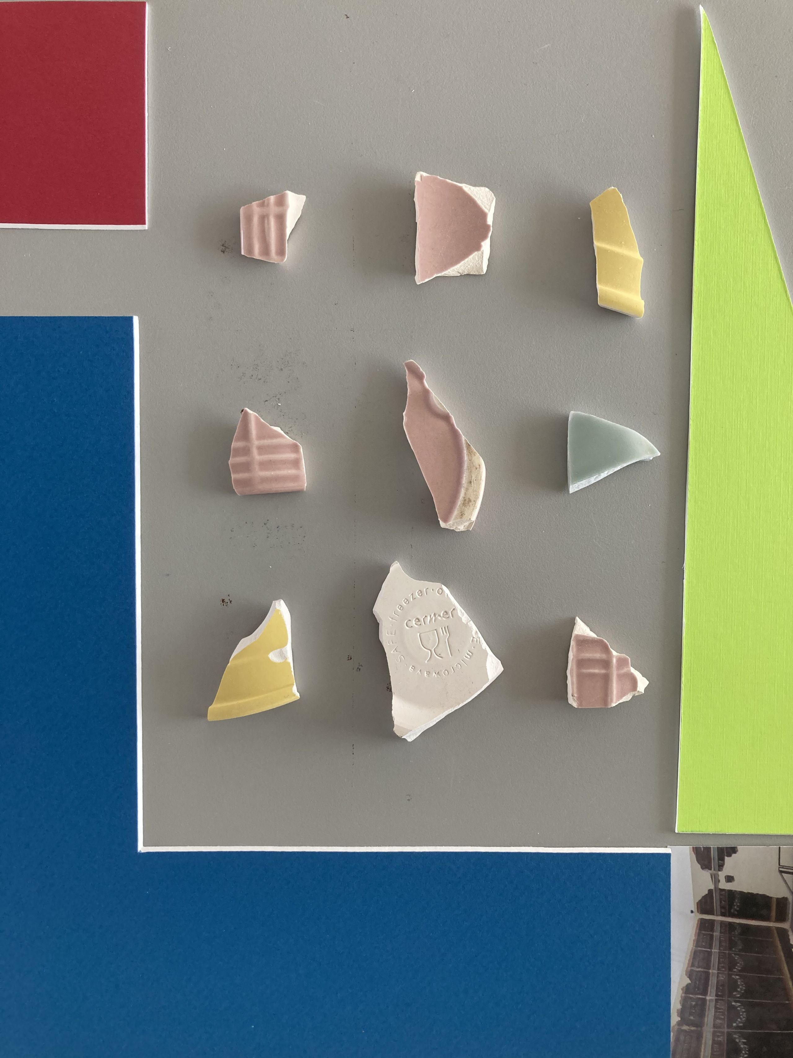Broken bits of ceramics, surrounded by coloured mountboard and the edge of a photograph