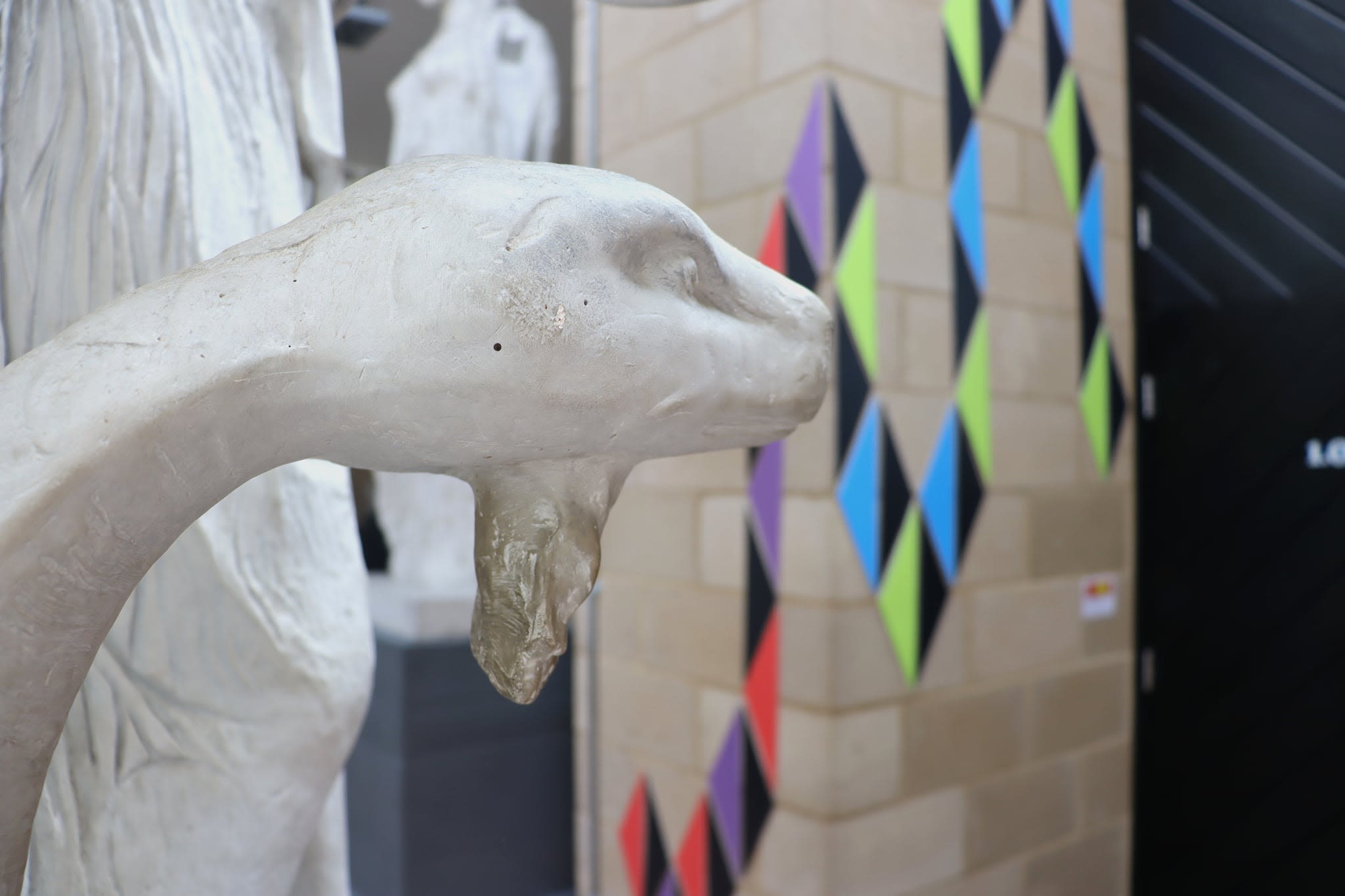 In the foreground is a statue of a snake, behind mountboard arranged in geometric pattern snakes its way up the wall.