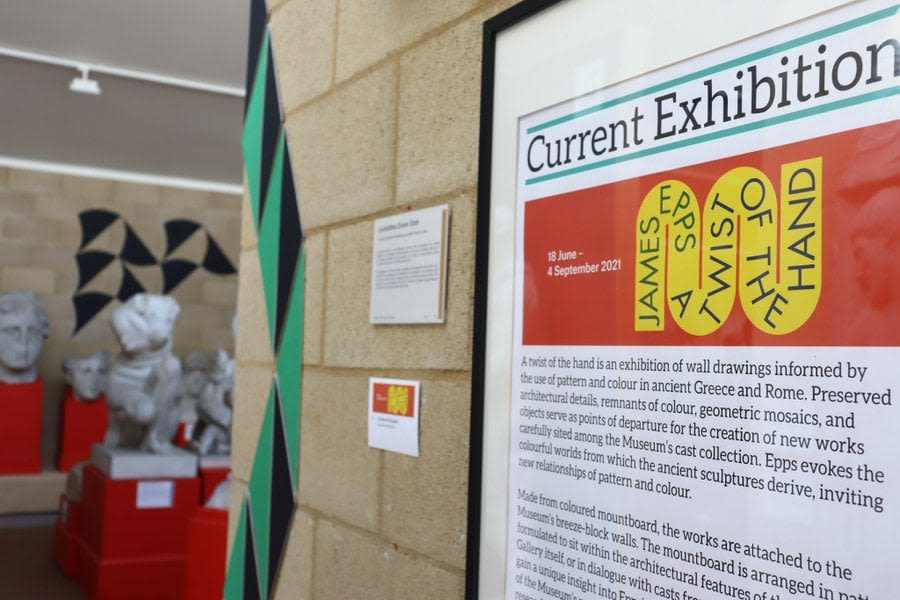 Exhibition intro panel with works in the background