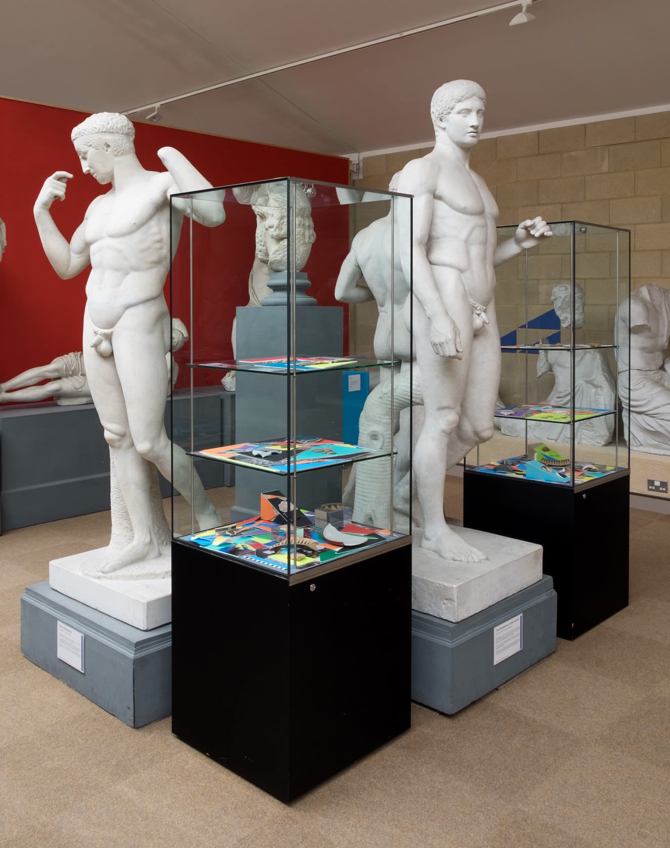Display cabinets in the gallery with colourful works inside, surrounded by plaster casts