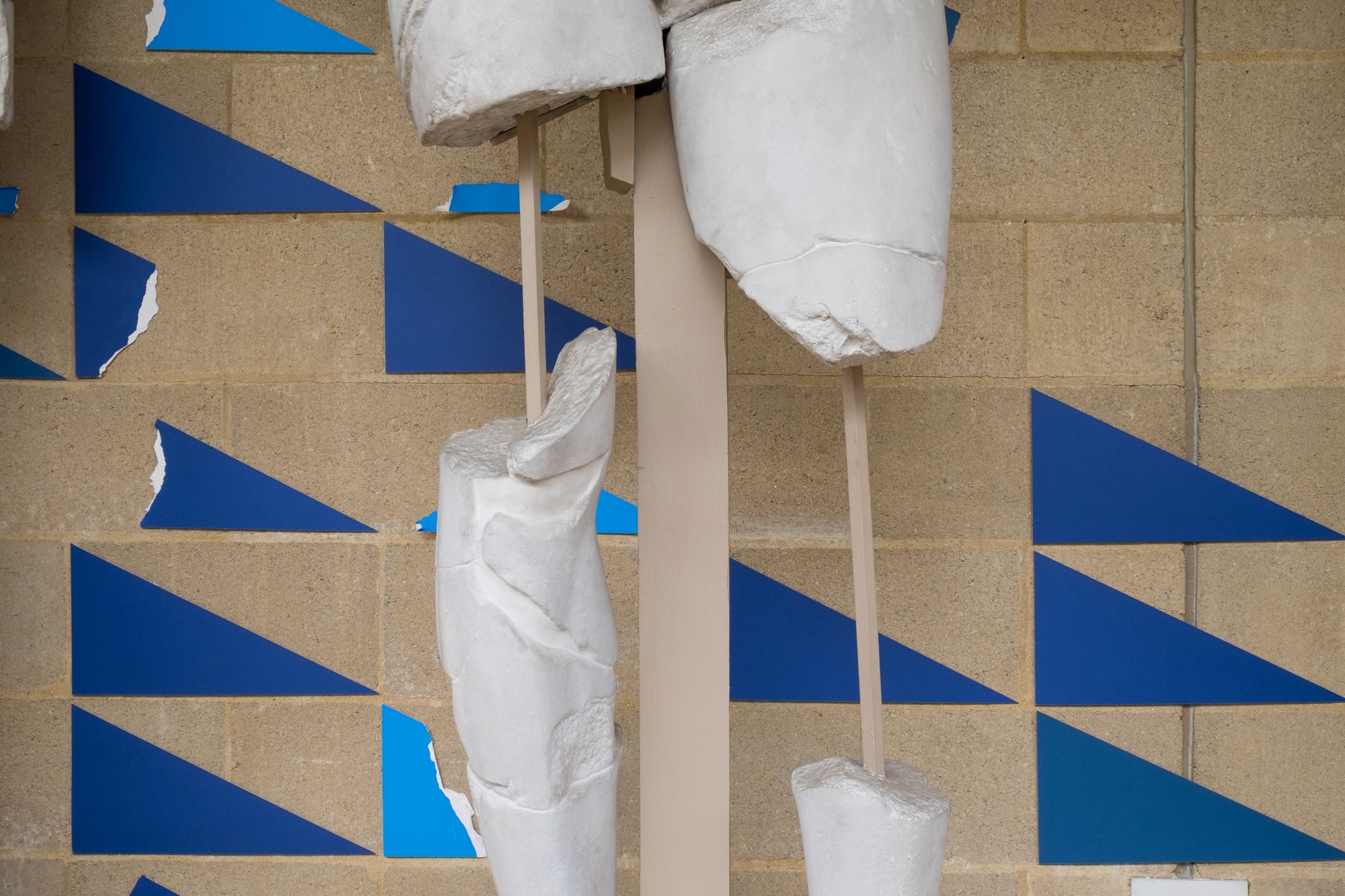 the fractured legs of a plaster cast in front of different shades of blue triangles, some are torn.