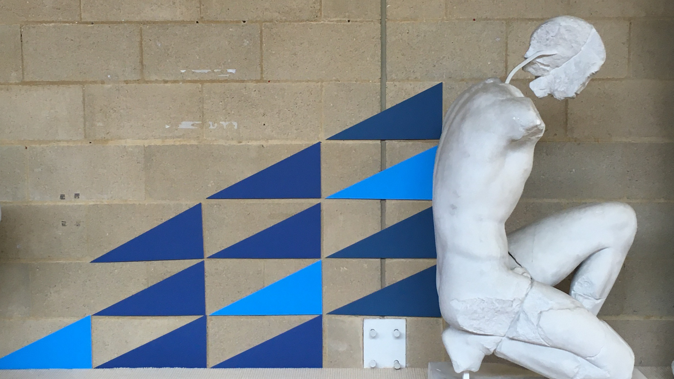 A cast of a crounching statue, James' blue triangles emerge from his back, with more continuing away from him.