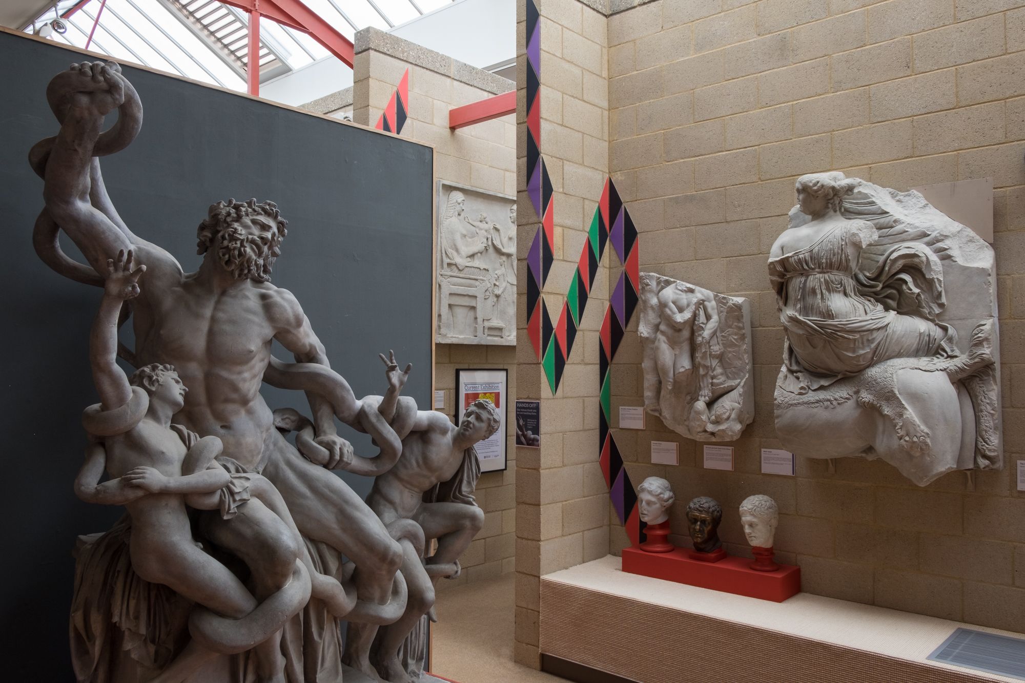 Plaster casts of the laocoon group in the museum of classical archaeology, to the right James Epps' geometric triangles curve and snake up the wall.
