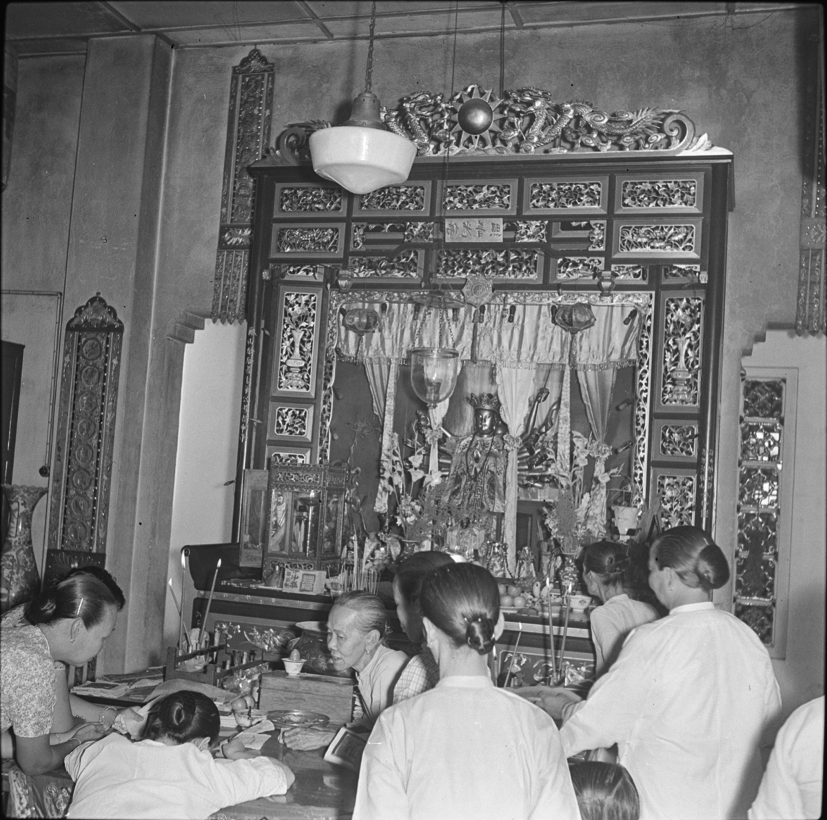 Elaborately carved wooden structure over the offering table houses the figure of an eight-armed deity, probably Guan Yin.