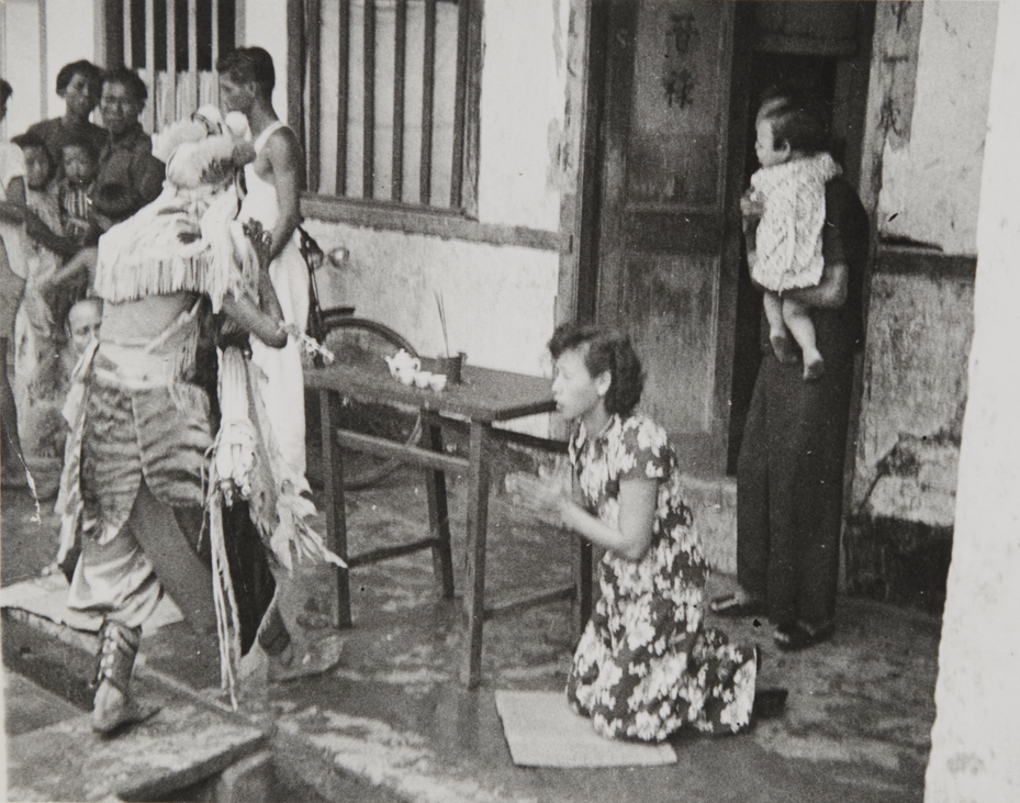 A woman kneels before a spirit-medium, at the entrance porch of a Chinese temple in Singapore