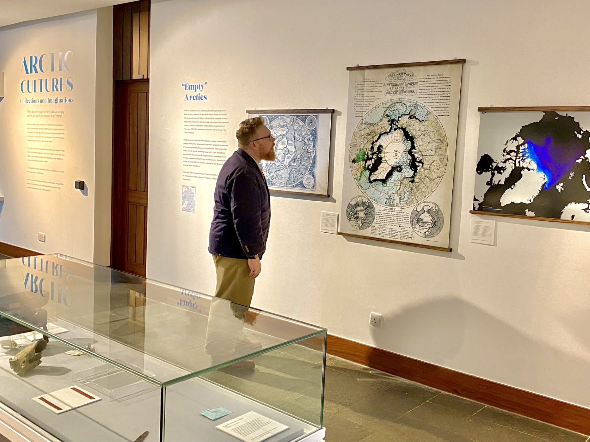 A bearded man stands in front of a map of the Arctic displayed on a wall at the Polar Museum.