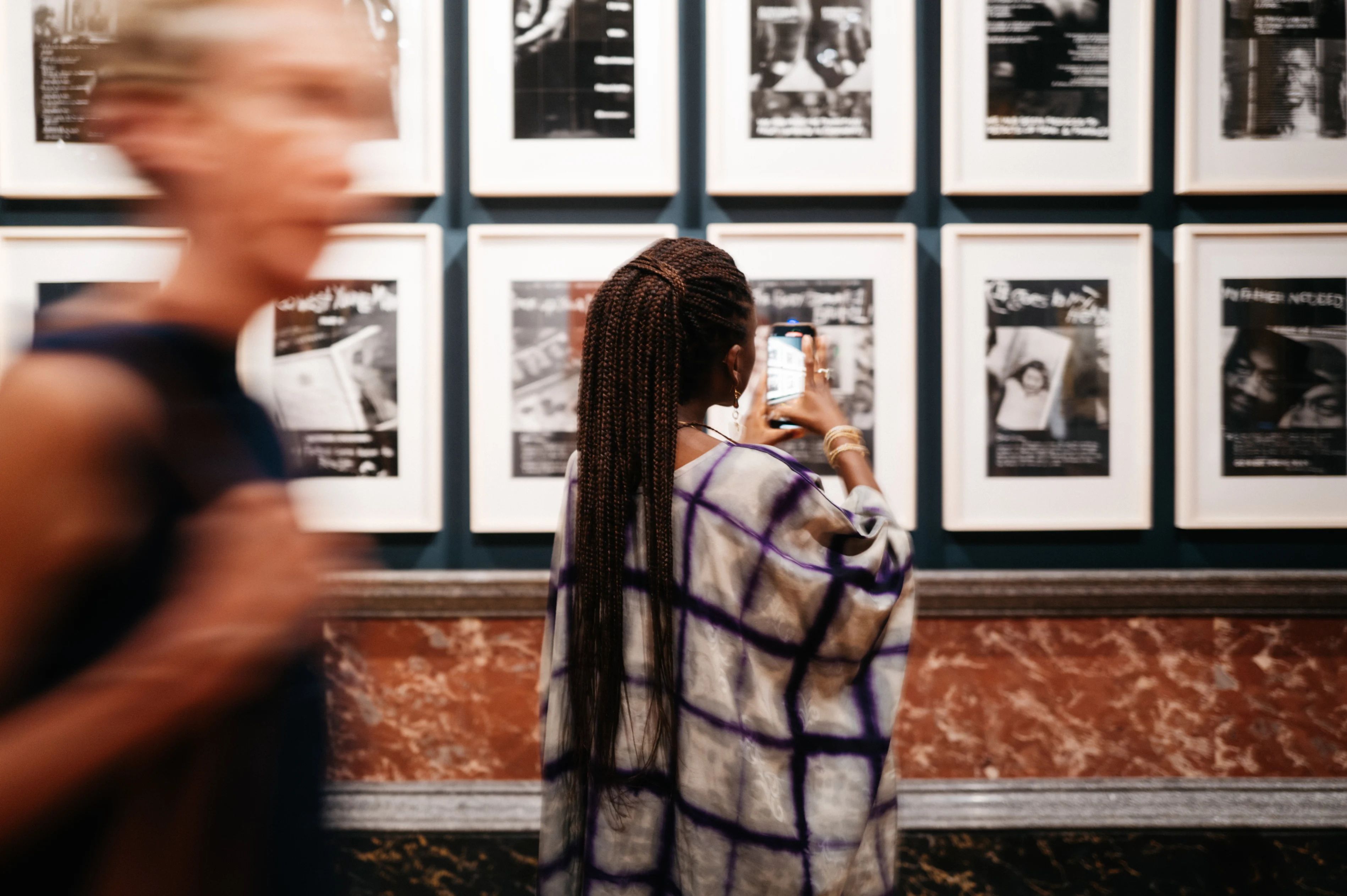 A woman with braids takes a picture of a wall of framed photographs at the exhibition.