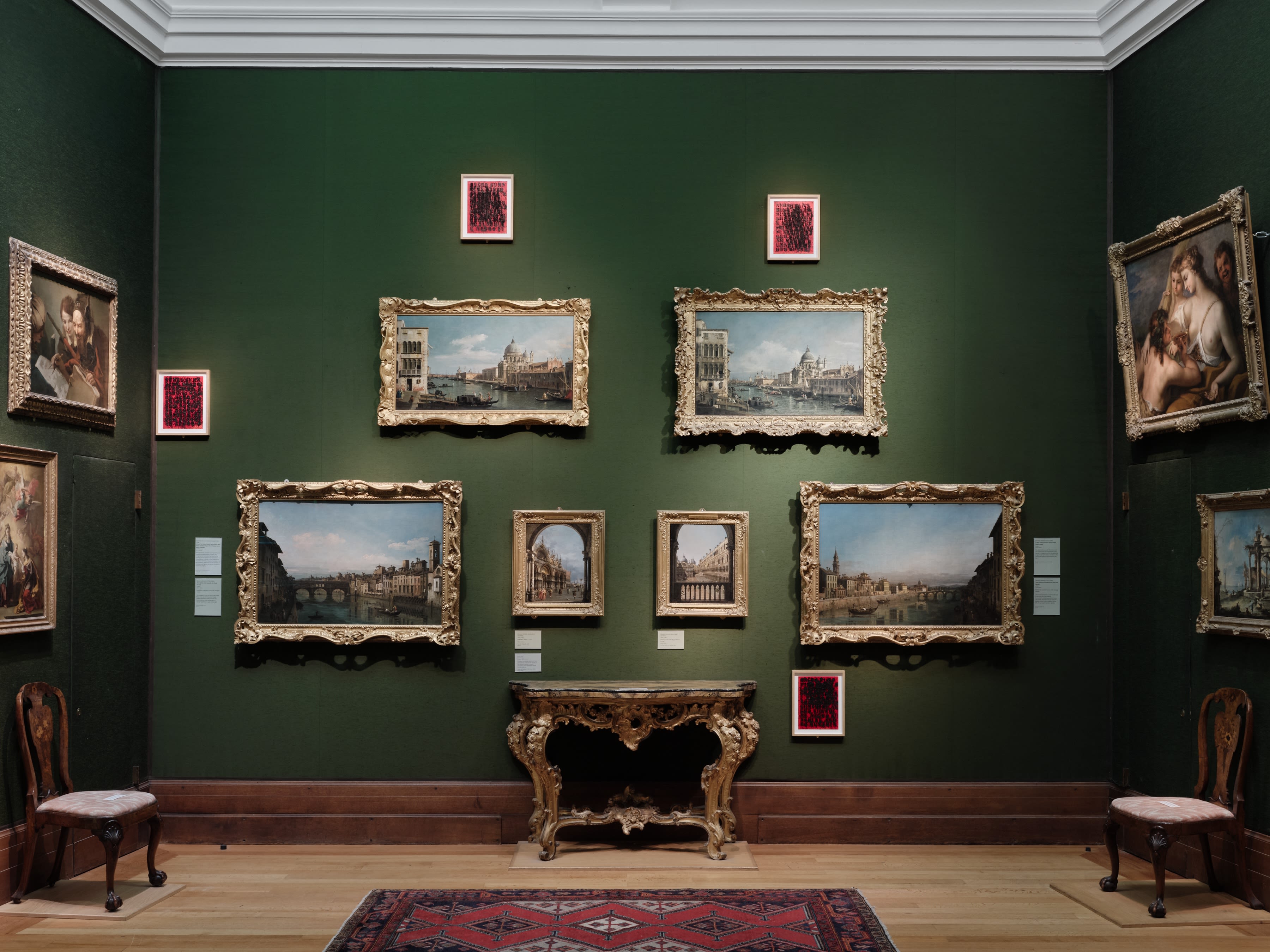A wall of gold framed landscape paintings at the Fitzwilliam Museum, surrounded by text prints as part of the Glenn Ligon exhibition.