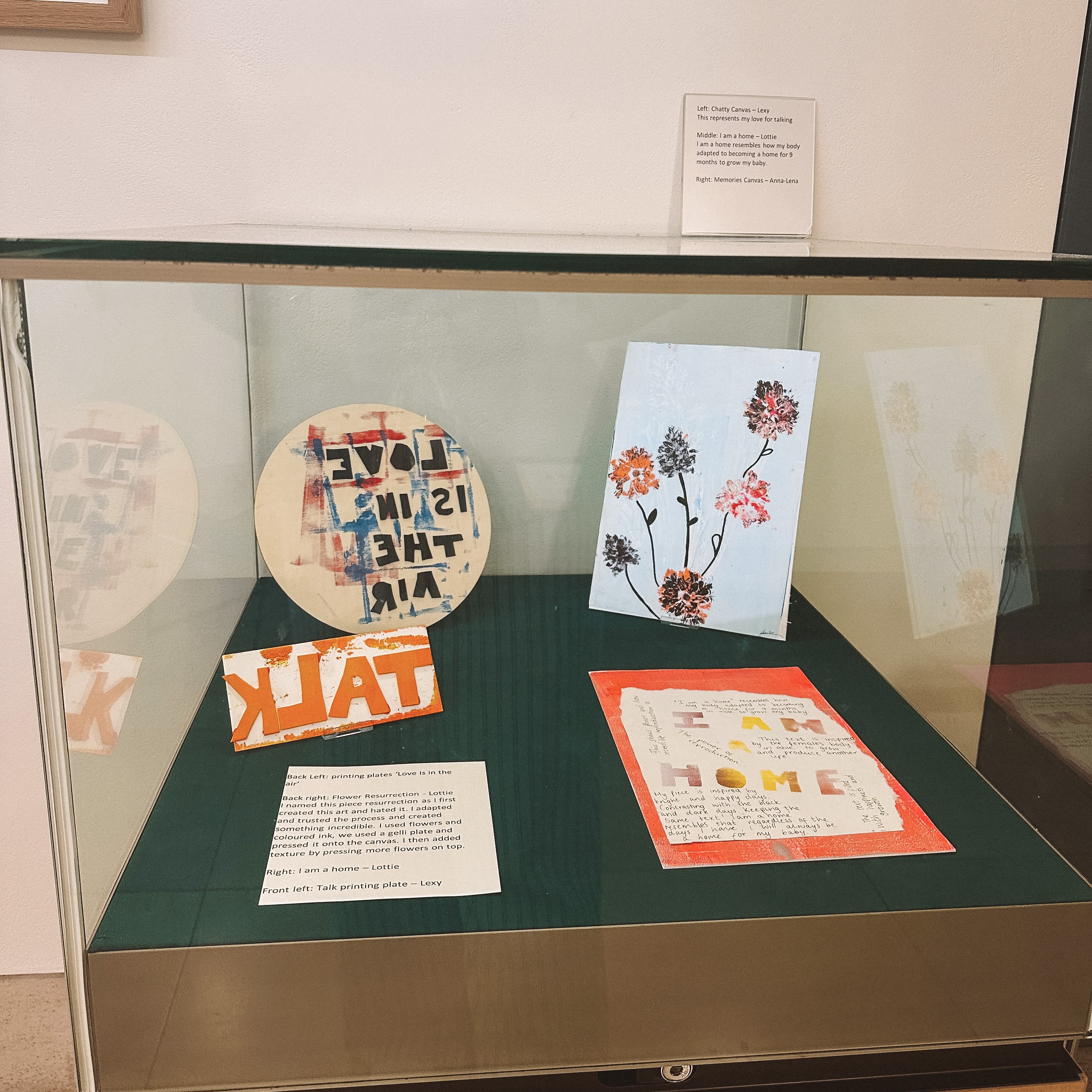 A glass display case filled with four artworks and label of the Young Parents group's work.