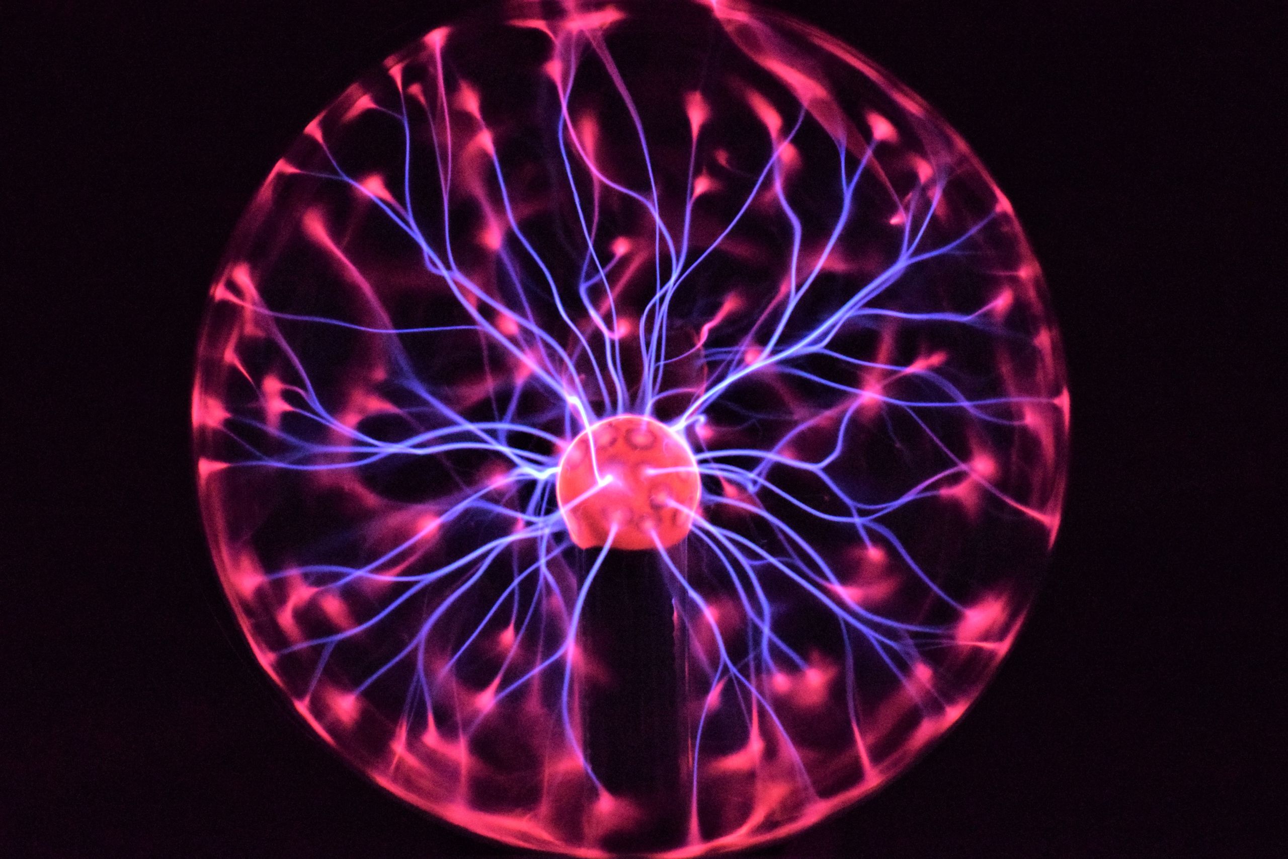 Plasma lamp with a pink centre sphere. Blue filaments extend between the inner and outer spheres casting pink spots around the edges of the glass.
