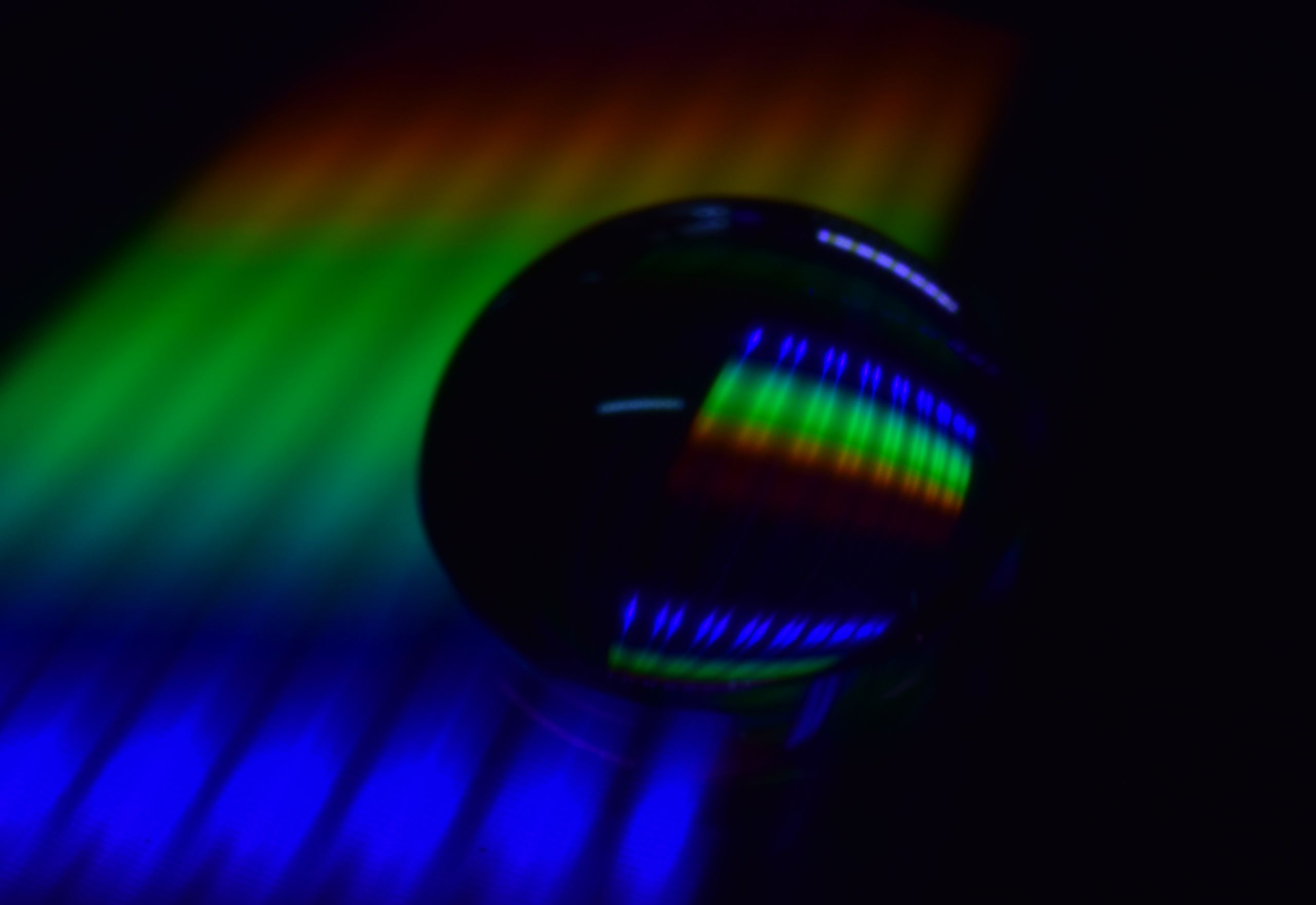 In the background are stripes of red bleeding into orange, the green the blues. In the foreground is a water droplet within which the background is reflected.