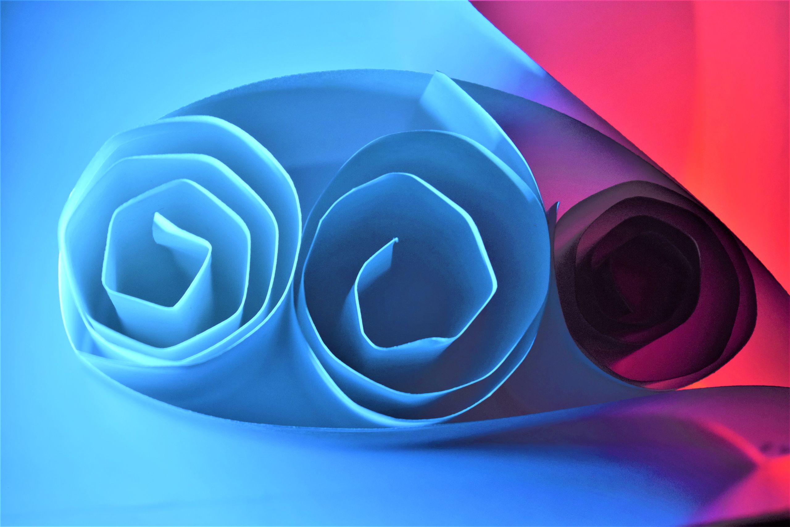 The ends of rolled up pieces of paper. They are lit by blue light from the left and red from the right, blending to cast a purple light in-between.